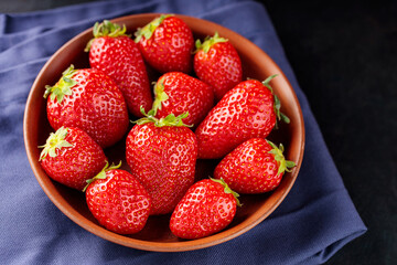 Fresh ripe strawberry in bowl on dark background. Clay bowl with strawberries on blue napkin. Copy space. Top view
