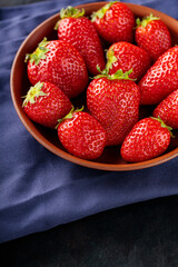 Fresh ripe strawberry in bowl on dark background. Clay bowl with strawberries on blue napkin. Copy space. Top view