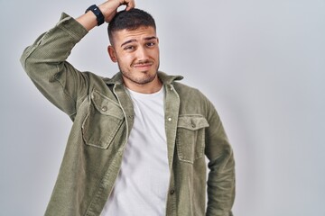 Young hispanic man standing over isolated background confuse and wondering about question....