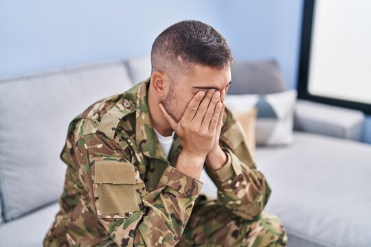 Young hispanic man army soldier sitting on sofa stressed at home