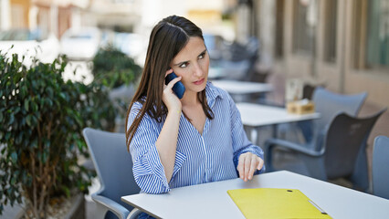 Young beautiful hispanic woman business worker talking on smartphone at coffee shop terrace
