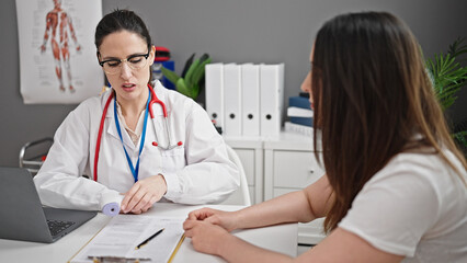 Fototapeta premium Two women doctor and patient using laptop having consultation at clinic