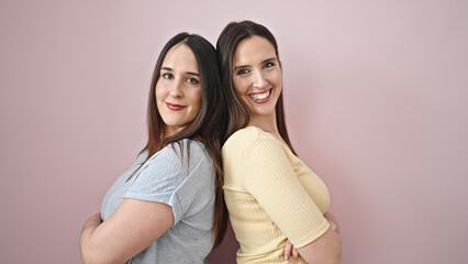 Two women smiling confident standing with arms crossed gesture over isolated pink background