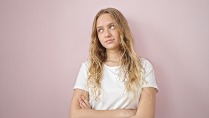 Young blonde woman looking to the side with serious expression and arms crossed gesture over isolated pink background