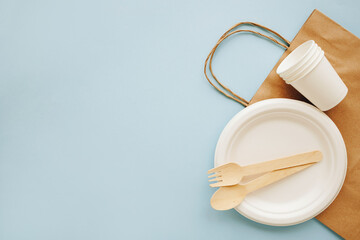 Eco-friendly disposable utensils made with wood and paper on a blue background. Spoons, fork, knives, bowls with paper cups and packet