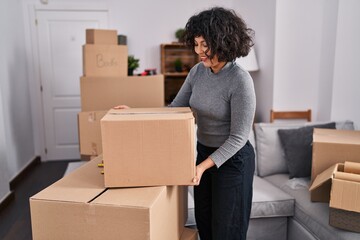 Fototapeta premium Young beautiful hispanic woman smiling confident holding package at new home