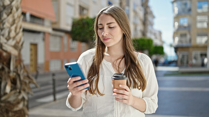 Young beautiful hispanic woman using smartphone drinking coffee at street