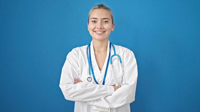 Young beautiful hispanic woman doctor smiling confident standing with arms crossed gesture over isolated blue background