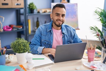 Young hispanic man artist using laptop drawing at art studio