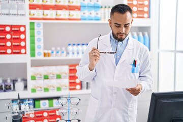 Young hispanic man pharmacist reading prescription at pharmacy