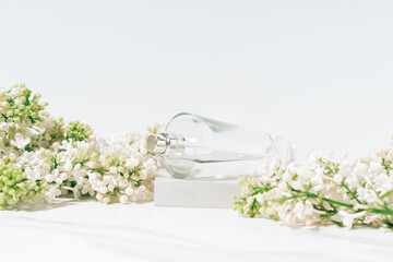 Minimal perfumery composition. Transparent perfume bottle and blossom branches on white background.