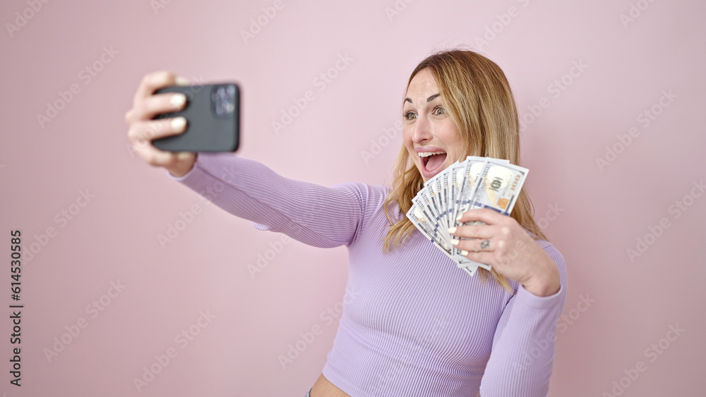 Sticker Young beautiful hispanic woman taking selfie holding dollars over isolated pink background