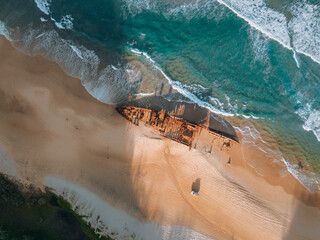 K'gari High angle aerial bird's eye drone view of the Maheno shipwreck on Seventy-Five Mile Beach on Fraser Island, Queensland, Australia. Beautiful sunset light with waves. - obrazy, fototapety, plakaty