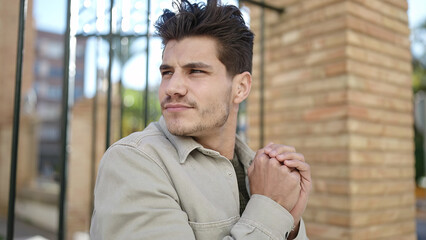 Young hispanic man rubbing hands for cold at street