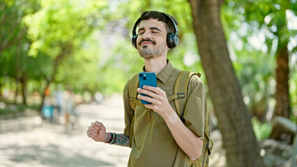 Young hispanic man tourist listening to music dancing at park