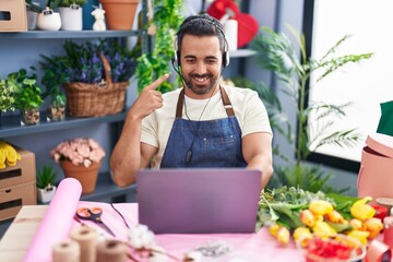 Hispanic man with beard working at florist shop using laptop smiling happy pointing with hand and finger