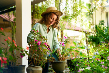 Young woman gardener in straw hat holding hand shovel taking care of potted plants. Junior...