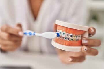 Young beautiful hispanic woman dentist teaching to clean tooth with brackets at clinic