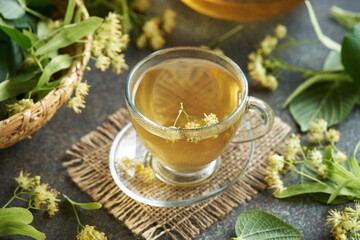A cup of herbal tea with linden flowers and leaves on a table