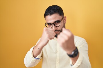 Hispanic young man wearing business clothes and glasses ready to fight with fist defense gesture, angry and upset face, afraid of problem