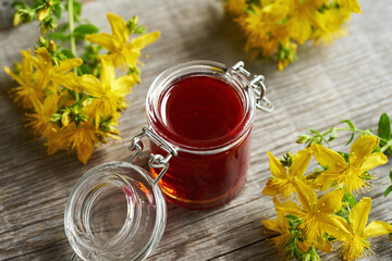 A jar of St John's wort oil with fresh Hypericum blossoms on a table