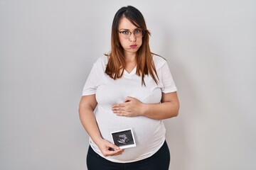 Pregnant woman holding baby ecography puffing cheeks with funny face. mouth inflated with air, catching air. - obrazy, fototapety, plakaty