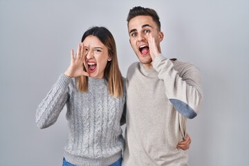 Young hispanic couple standing over white background shouting and screaming loud to side with hand on mouth. communication concept.