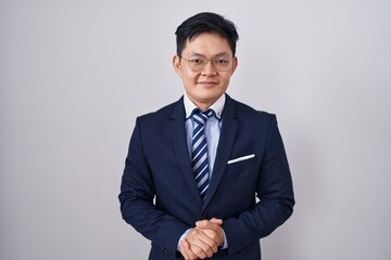Young asian man wearing business suit and tie with hands together and crossed fingers smiling relaxed and cheerful. success and optimistic