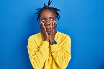 Beautiful black woman standing over blue background tired hands covering face, depression and sadness, upset and irritated for problem
