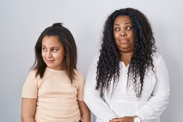 Mother and young daughter standing over white background smiling looking to the side and staring away thinking.