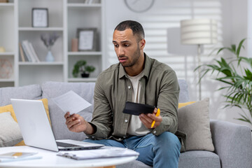 Young african american freelancer businessman working remotely from home with laptop and documents....