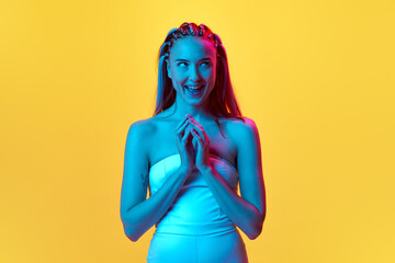 Making joyful plan. Portrait of pretty young woman with funny thoughtful face standing against yellow studio background in neon light. Concept of youth, emotions, beauty, lifestyle, ad