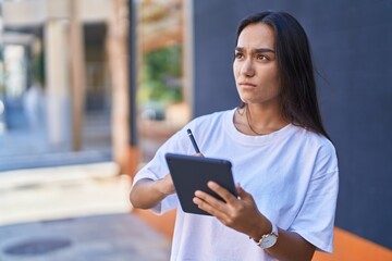 Fototapeta premium Young beautiful hispanic woman drawing on touchpad at street