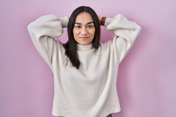 Young south asian woman standing over pink background relaxing and stretching, arms and hands behind head and neck smiling happy