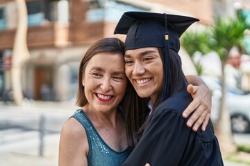 Two women mother and graduated daughter hugging each other at street