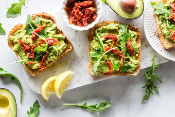 Healthy avocado and arugula toast topped with sun dried tomatoes.