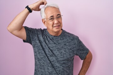 Middle age man with grey hair standing over pink background confuse and wondering about question. uncertain with doubt, thinking with hand on head. pensive concept.