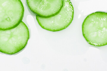 Thinly sliced slices of fresh green cucumber on a background of spilled green clear liquid.