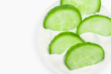 Slides of fresh cucumber in a jar of cream. On a white background.