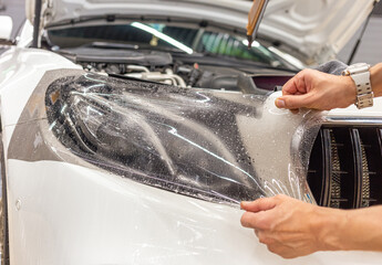 The process of installing a protective polyurethane film for paint on the front headlight of a car. PPF is a polyurethane film that helps protect glass and metal from scratches.  - obrazy, fototapety, plakaty