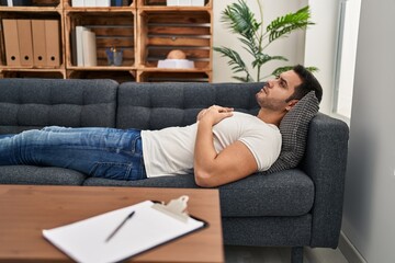Young hispanic man stressed having mental therapy lying on sofa at psychology center - obrazy, fototapety, plakaty