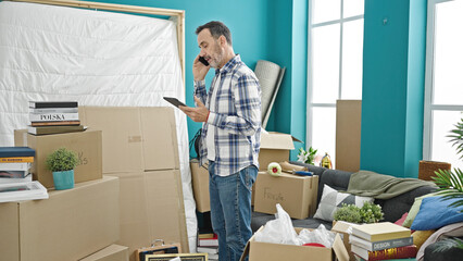 Middle age man talking on smartphone using touchpad at new home