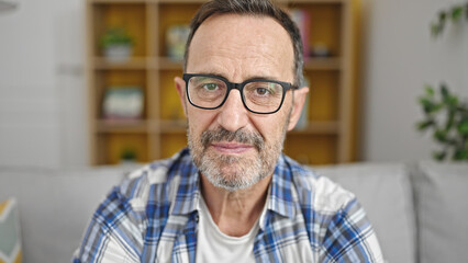 Middle age man sitting on sofa with relaxed expression at home