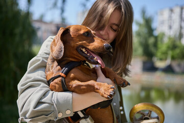 Loving owner carrying a handicapped dog outdoors. Portrait of a cheerful young girl with the...