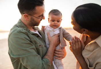 Loving young parents enjoying family tender moments with little infant son outside, walking on...