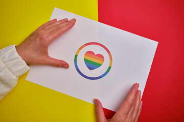 Rainbow heart from paper in woman hands. LGBT flag. LGBTQIA Pride Month in June. Lesbian Gay...