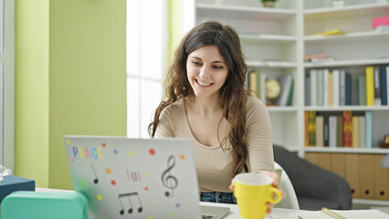 Young beautiful hispanic woman student using laptop drinking coffee at library university