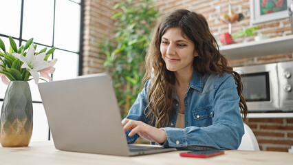 Young beautiful hispanic woman using laptop sitting on table at dinning room