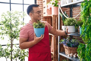 Young chinese man florist holding plant at florist