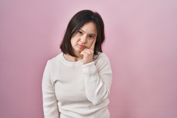 Woman with down syndrome standing over pink background with hand on chin thinking about question, pensive expression. smiling and thoughtful face. doubt concept.